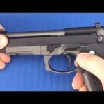 Hands shown beginning to field strip a Beretta 92FS with the slide locked in place.